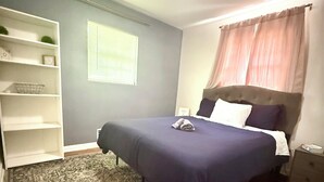 Un dormitorio con una cama, una mesita de noche, una estantería, una ventana con persianas y una alfombra estampada.