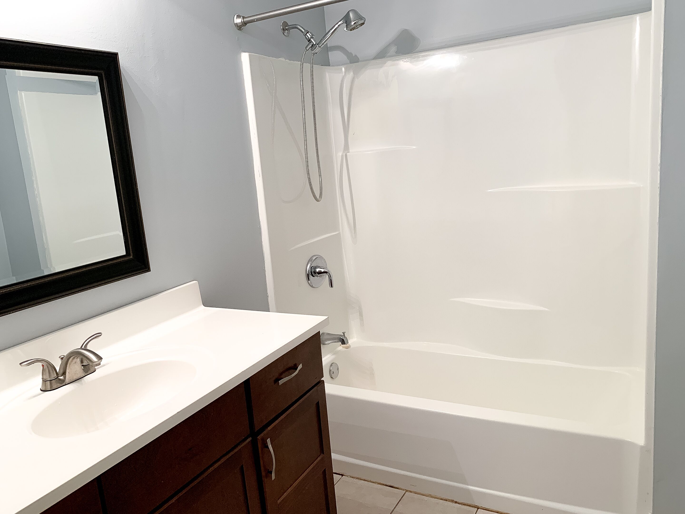 Une salle de bain avec une baignoire blanche, un lavabo avec un miroir et une douche équipée d’un pommeau de douche à main.
