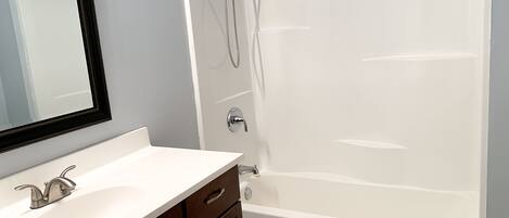 Une salle de bain avec une baignoire blanche, un lavabo avec un miroir et une douche équipée d’un pommeau de douche à main.
