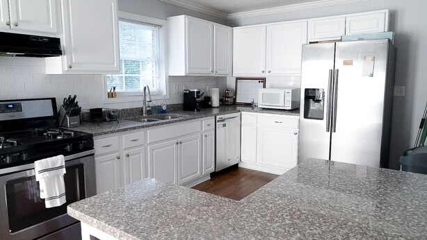 Una cocina con armarios blancos, un refrigerador de acero inoxidable, un microondas, una estufa y un lavabo.