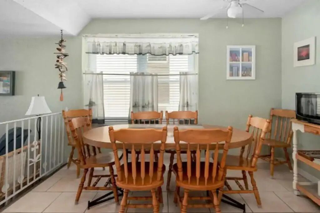 Un comedor con una mesa redonda y sillas de madera, un ventilador de techo y una ventana con cortinas.