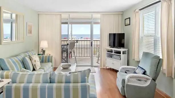 Un soggiorno con divano, poltrone, televisore e un balcone vista spiaggia.