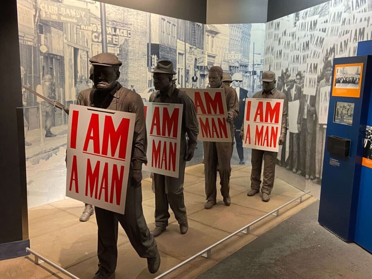 Une exposition de musée présentant des statues tenant des panneaux sur lesquels on peut lire : « Je suis un homme ».