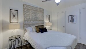 Une chambre à coucher avec un grand lit, un papier peint à motifs, deux lampes de chevet et un ventilateur de plafond.