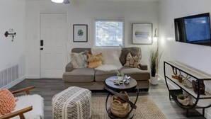 Un salon avec un canapé gris, une table basse, un téléviseur fixé au mur et un ventilateur de plafond.