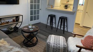 Un salon comprenant un téléviseur, une table ronde, deux tabourets de bar et un canapé.