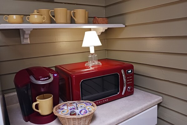 A kitchenette with a red microwave, a Keurig coffee maker, a coffee cup, and a basket of yogurt cups.