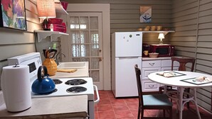 A compact kitchen with a stove, microwave, refrigerator, and a dining table with chairs. - Private Garden, Jacuzzi Tub, Fireplace, In-Cottage Breakfast & Walking Distance to SoMa Are Just the Beginning! (Little Rock)