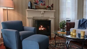 A living room with a fireplace, a blue armchair, a glass coffee table, and a sofa. - Private Garden, Jacuzzi Tub, Fireplace, In-Cottage Breakfast & Walking Distance to SoMa Are Just the Beginning! (Little Rock)