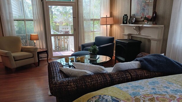 A cozy room with a bed, a chair, a table with a lamp, and a fireplace. - Private Garden, Jacuzzi Tub, Fireplace, In-Cottage Breakfast & Walking Distance to SoMa Are Just the Beginning! (Little Rock)
