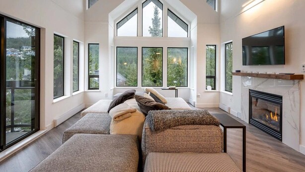 A modern living room with a fireplace, large windows, and a television. - Luxury | Mountain views | Free parking | AC | BBQ (Whistler)