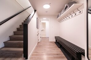 Un escalier avec une rampe, un banc, un porte-manteau et une porte donnant sur une autre pièce.