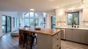 A modern kitchen with a central island, bar stools, and large windows offering views of the outdoors. - Luxury | Mountain views | Free parking | AC | BBQ (Whistler)