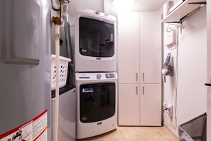 Une buanderie équipée d’une laveuse et d’une sécheuse superposées, d’un étendoir et d’un aspirateur fixé au mur.