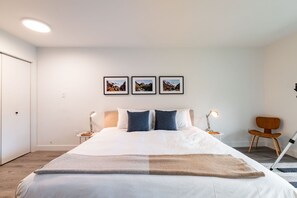 Une chambre à coucher moderne avec un grand lit, deux lampes de chevet, un fauteuil et trois tableaux encadrés accrochés au mur.