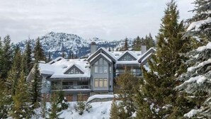 A large, multi-story lodge with a symmetrical design, surrounded by snow-covered trees and mountains in the background. - Luxury | Mountain views | Free parking | AC | BBQ (Whistler)