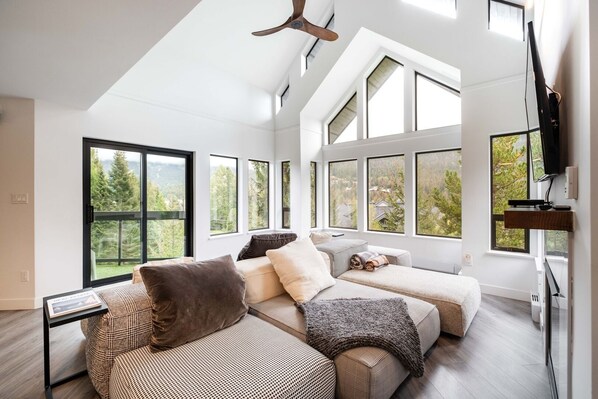 Una sala de estar moderna con techo alto, ventanas amplias y televisor de pantalla plana.