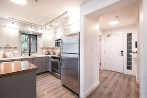 A modern kitchen with stainless steel appliances, a wooden countertop, and white cabinetry.