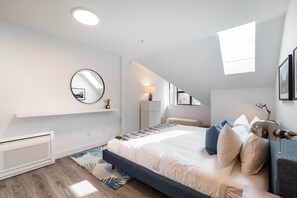 A modern bedroom with a large bed, a round mirror, a desk, and a window.