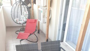 A balcony with wicker furniture, a red chair, and a glass table. - 2-bed - Sleeps 4 - With Parking (Blagoevgrad)