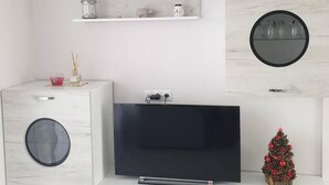 A modern living room with a flat-screen TV, a small Christmas tree, and a round mirror on the wall. - 2-bed - Sleeps 4 - With Parking (Blagoevgrad)