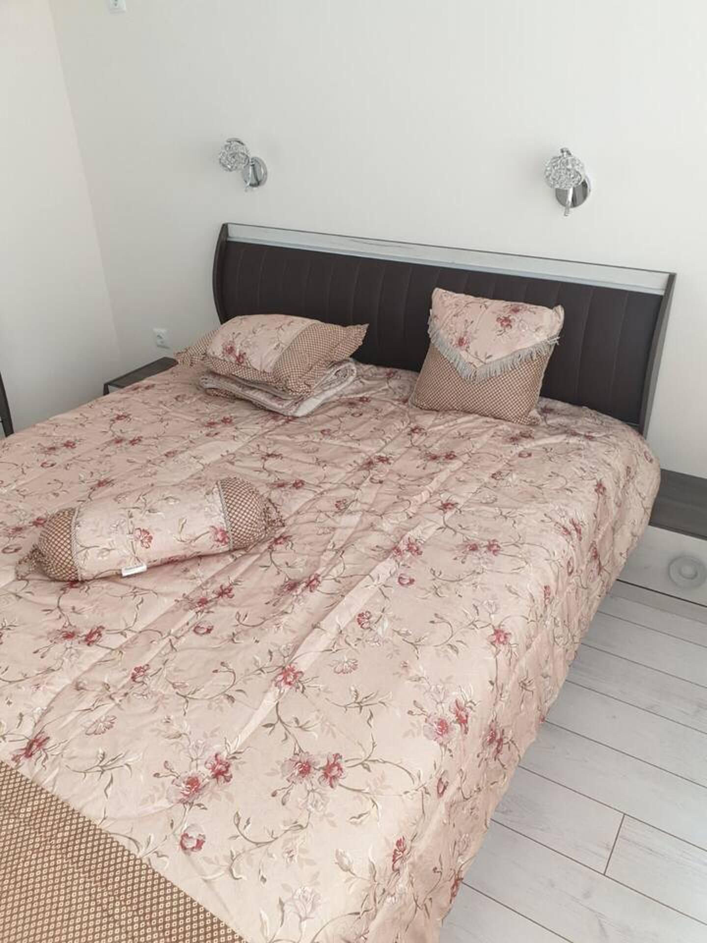A neatly made bed with floral bedding and two pillows, a dark headboard, and a small bedside table with a lamp.