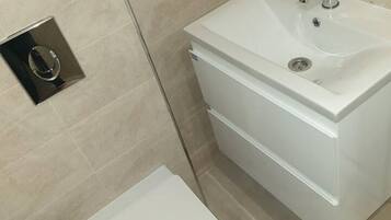 Un baño moderno con un lavamanos, inodoro y toallero blancos.