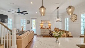 A spacious living room with a marble dining table, a sofa, and a kitchen area with a clock and decorative items. - Escapeto30A/GolfCartIncluded/Pool/WalkToBeach (Santa Rosa Beach)