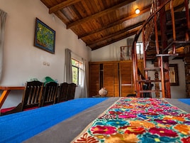 Una habitación con techo de madera, una alfombra colorida, una escalera y un cuadro en la pared.