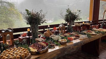Una larga mesa de madera dispuesta con diversos alimentos y una vela, con vistas a árboles.