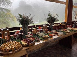 A long wooden table set with various food items and a candle, with a view of trees outside.