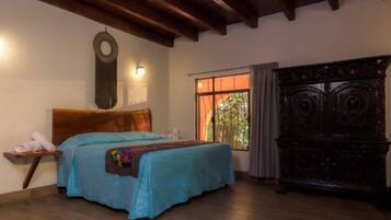 Un dormitorio con cama de madera, una mesita de noche, una lámpara de pared, una ventana con cortinas y un aparador de madera oscura.