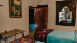 A room with a bed, a desk, a chair, a door, and a painting on the wall. - Hotel Boutique Finca de la Niebla Coatepec (Tlalnelhuayocan)
