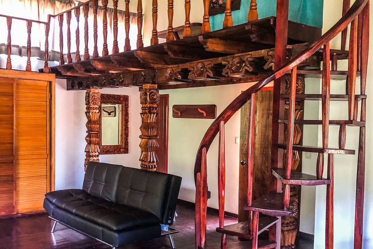 Uma sala de estar ampla com um sofá de couro preto, uma escada de madeira com detalhes entalhados e teto de madeira.