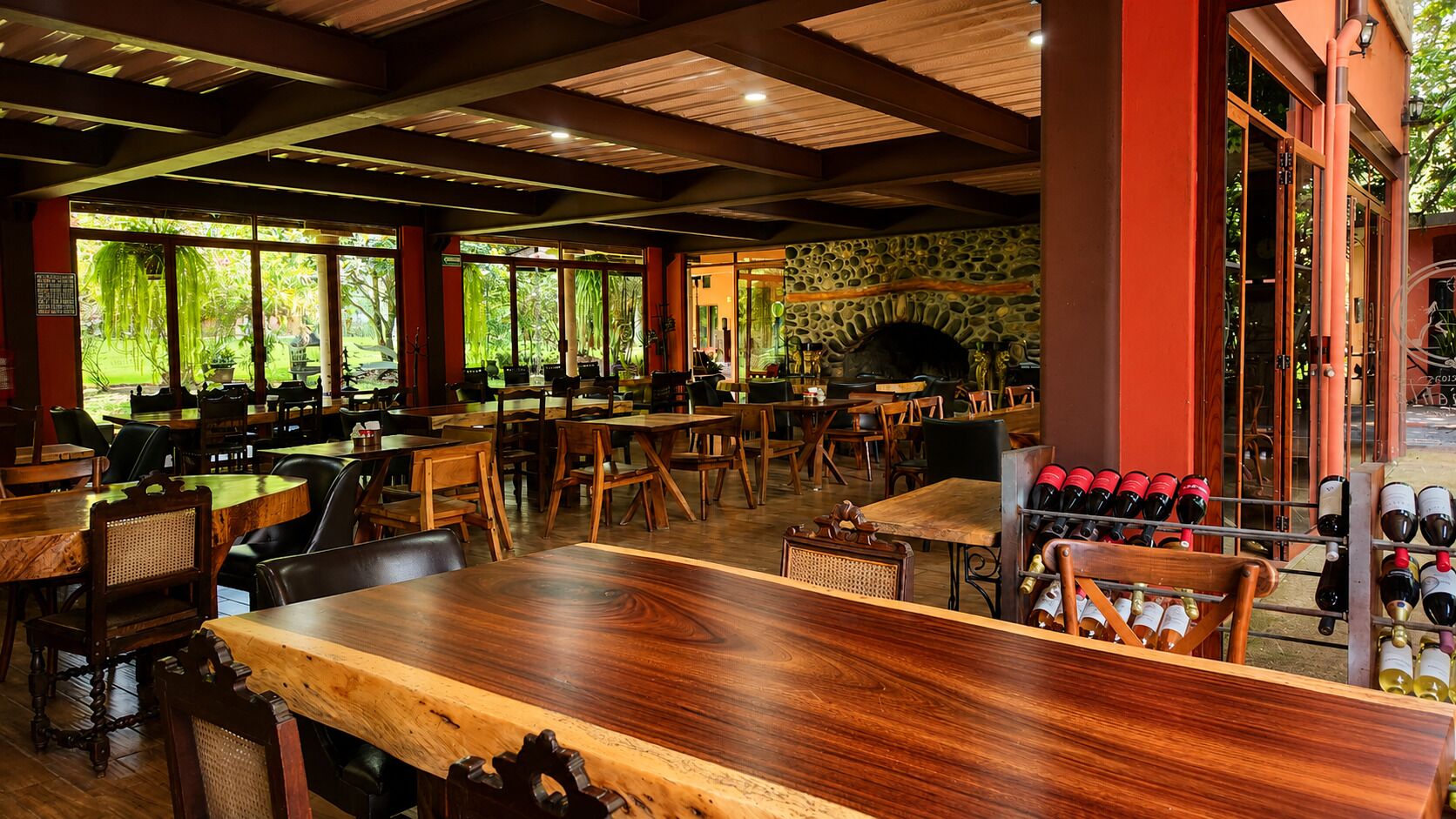 Un restaurante interior con mesas y sillas de madera, una pared de piedra y una estantería para vinos.