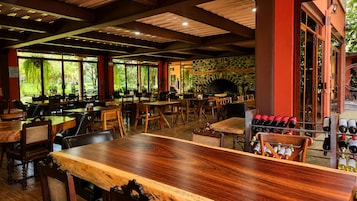 Un restaurante interior con mesas y sillas de madera, una pared de piedra y una estantería para vinos.