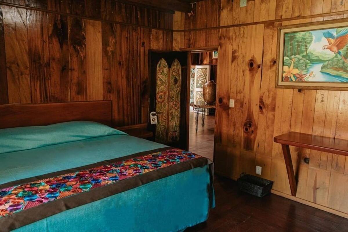 Um quarto de madeira com uma cama, uma porta que dá para outro espaço e um quadro na parede.