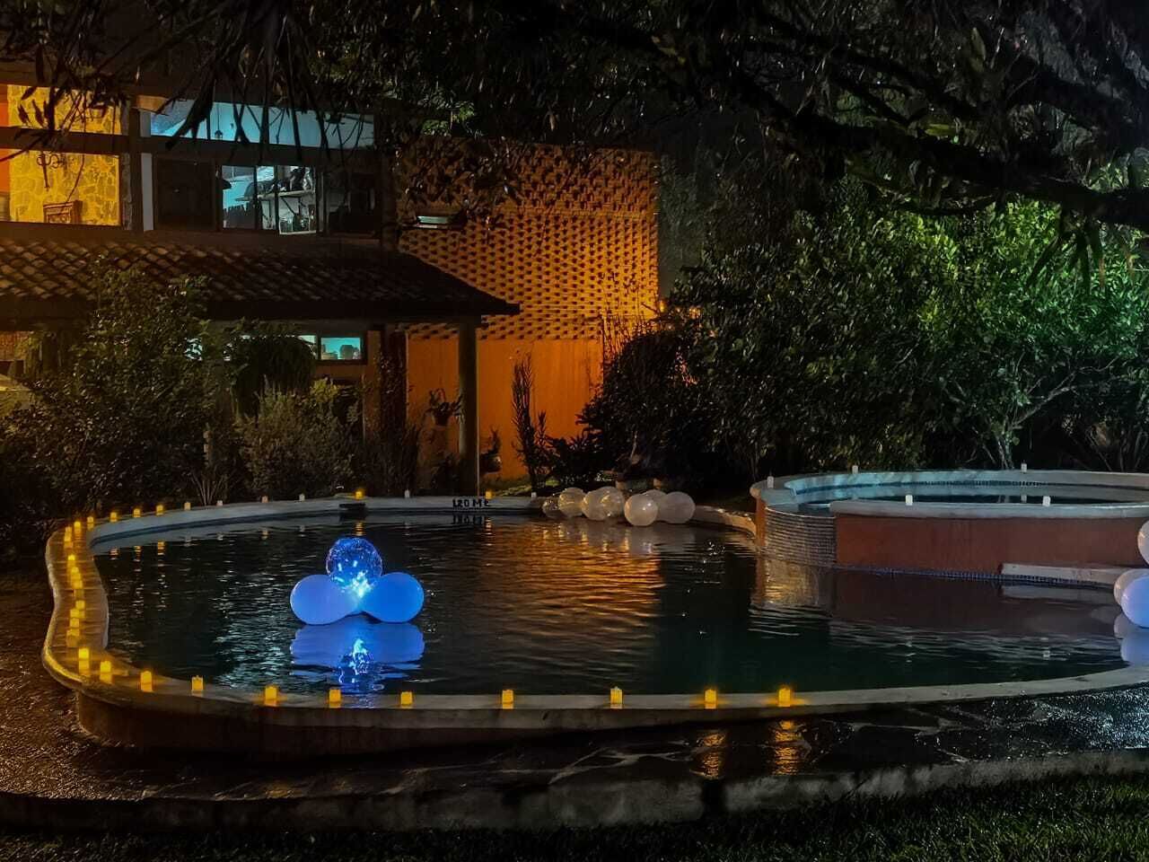 Piscina con una fuente y un jacuzzi, rodeada por una valla y árboles.