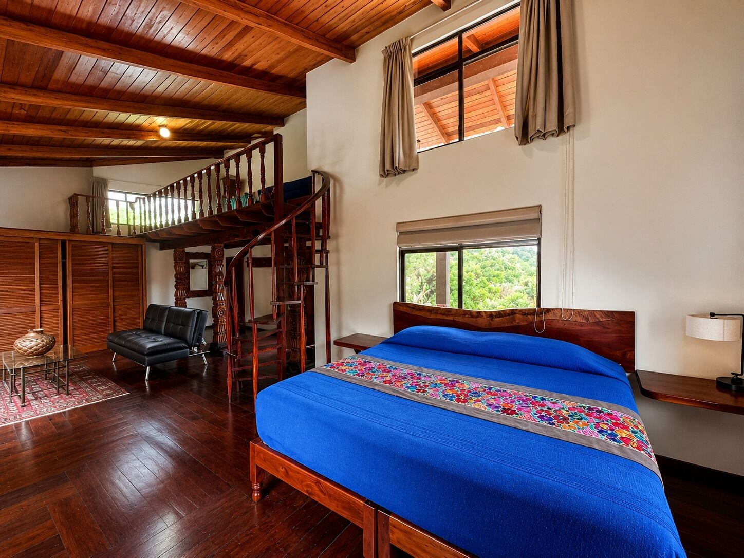A bedroom with a wooden bed, a staircase, a chair, and a window with curtains.