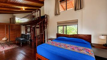 A bedroom with a wooden bed, a staircase, a chair, and a window with curtains.