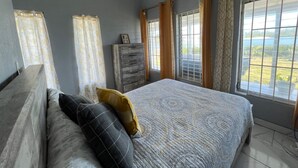 Quarto com uma cama, cômoda e janela com cortinas.
