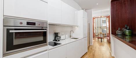 Una cocina moderna con armarios blancos, horno empotrado y cafetera.