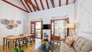 Amplia sala de estar con una mesa de comedor de madera, un sofá y una mesa de centro. Hay platos decorativos en la pared, un televisor y un balcón con vistas.