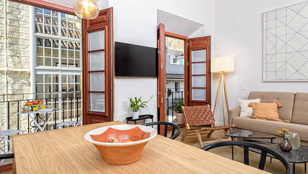 Una sala de estar con una mesa de comedor de madera, un sofá y un televisor montado en la pared.