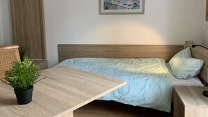 Une chambre à coucher avec un lit, une tête de lit en bois, une petite table avec une plante, une armoire et un tableau au mur.