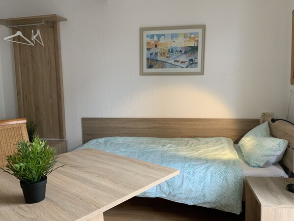A bedroom with a bed, a wooden headboard, a small table with a plant, a wardrobe, and a painting on the wall. - Room for fitters with shared bathroom and balcony (Weiterstadt)