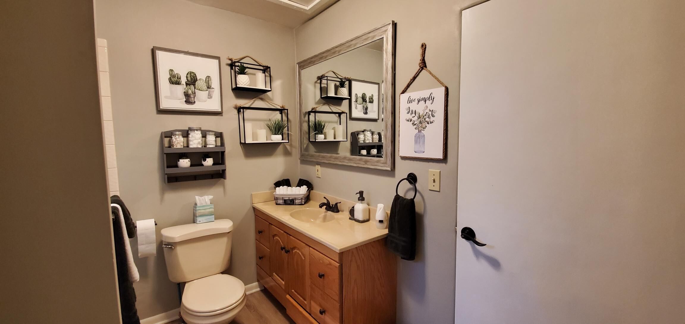 Een badkamer met toilet, wastafel, planken met planten, een spiegel en een bord met de tekst 'eenvoudig leven'.