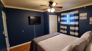 A bedroom with a bed, a ceiling fan, a TV, and a window with striped curtains. - Charming rental within walking distance to public boat launch on Sage Lake! (Hale)
