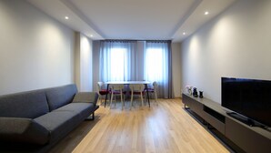 A modern living room with a grey sofa, a dining table with four chairs, a flat-screen TV, and a wooden floor. - Brand new apartment in the heart of Udine (Udine)