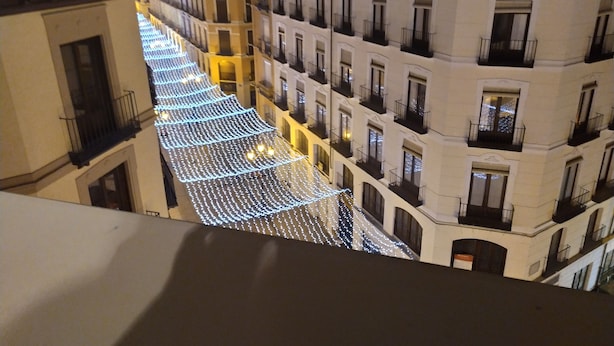A row of buildings with balconies and a street covered with string lights.